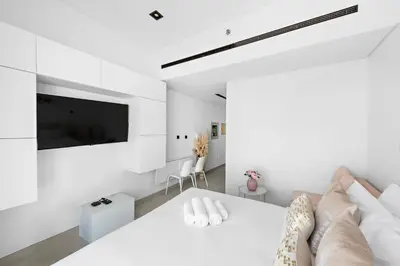a white bedroom with a large bed and a flat screen tv at Stylish Studio with Gym and Pool in Dubai