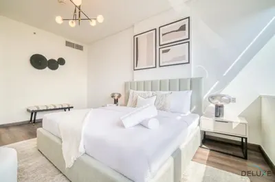 a white bedroom with a large white bed and a chair at Amazing 2BR at Sky Gardens DIFC by Deluxe Holiday Homes in Dubai