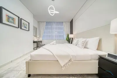 a white bedroom with a large bed and a desk at Limited Time Offer Stylish 1BR near to Metro by Deluxe Holiday Homes in Dubai