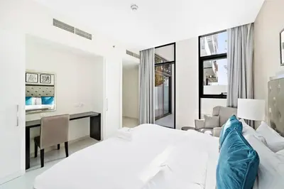 a white bedroom with a bed and a desk at StoneTree - Furnished 1BR minutes of drive away to Expo 2020 in Dubai