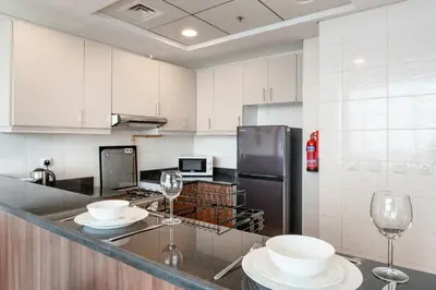 a kitchen with white cabinets and white plates and wine glasses at Studio in Reef Residence JVC by PK Holidays in Dubai