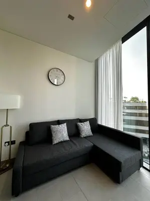 a black couch in a room with a clock on the wall at Prime 1BR in Sobha Hartland, Burj Khalifa view in Dubai