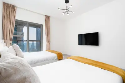 a white bedroom with two beds and a tv at Lux BnB Princess Tower Palm Ocean Views in Dubai