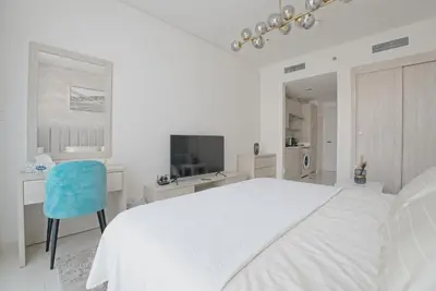 a white bedroom with a large bed and a blue chair at Luxury Studio, Seven Palm Residence-Palm Jumeirah in Dubai