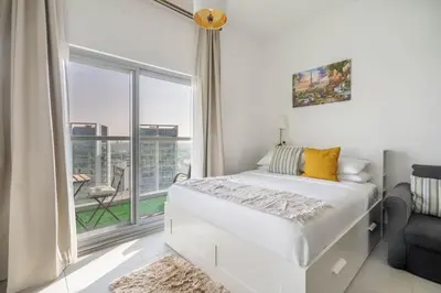 a white bedroom with a bed and a large window at GuestReady - Bella Rose residence in Dubai in Dubai