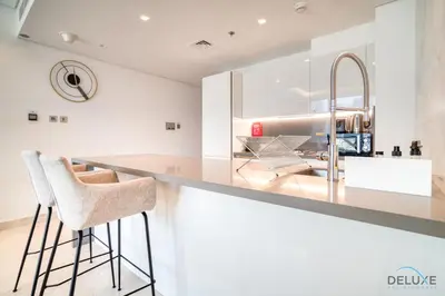 a kitchen with white cabinets and a counter with stools at Burj Khalifa Views! Promo on 1BR at Sterling House by Deluxe Holiday Homes in Dubai