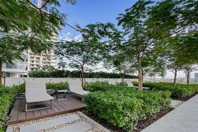 a patio with two chairs and a table and trees at Trophy - Marina Vista Sea View Suite in Dubai