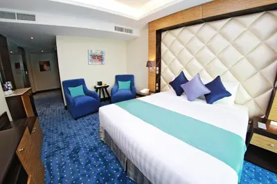 a bedroom with a large bed and two blue chairs at Armada Avenue Hotel in Dubai