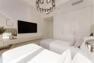 a white bedroom with two beds and a flat screen tv at Daniels 2BR at Downtown with Burj Khalifa View in Dubai