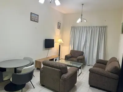 a living room with chairs and a table and a tv at Stylish 1bhk at silicon oasis in Dubai