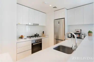 a kitchen with white cabinets and a stainless steel refrigerator at Ahad Residences - City Retreat Apartments - Zed Living in Dubai