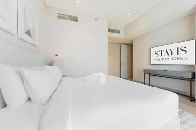 a white bedroom with a white bed and a desk at Stayis -Luxurious 2BR Apartment with breathtaking ocean and Marina View in Dubai