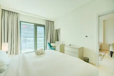 a white bedroom with a white bed and a window at Seven Palm 1 Bed with Rooftop Infinity Pool in Dubai
