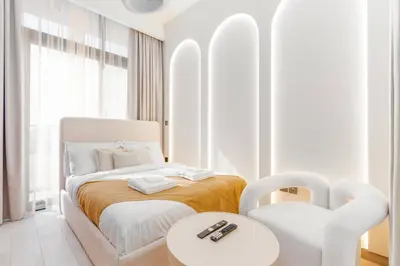 a white bedroom with a bed and two chairs at Studio 12min from Burj Khalifa - Azizi Riviera 32 - Dubai in Dubai