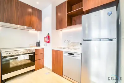 a kitchen with a stainless steel refrigerator and wooden cabinets at Magnificent 2BR at La Voile Jumeirah by Deluxe Holiday Homes in Dubai