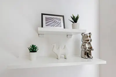 a white shelf with a picture and plants on it at Luxurious Flat 3 Min to Burj Khalifa Sleeps 3 in Dubai