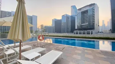 a pool with chairs and an umbrella on a building at Business Bay Gem1 bd apt with Scenic Canal Views in Dubai