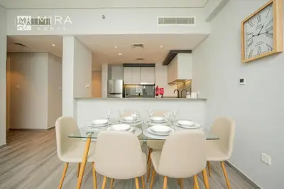 a dining room with a glass table and white chairs at Mira Holiday Homes - Spacious 2 bedroom in Midtown in Dubai