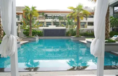 a swimming pool with palm trees and a building at Cosy 1BR in the center of JVC in Dubai