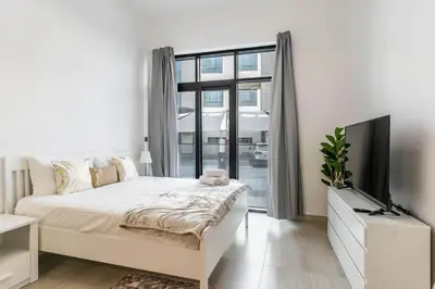 a white bedroom with a bed and a flat screen tv at HAVN - Studio Apartment in Pantheon Elysee, JVC in Dubai
