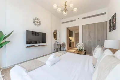 a white bedroom with a white bed and a clock at HAVN - Smart Home Studio in Oxford 212, JVC in Dubai