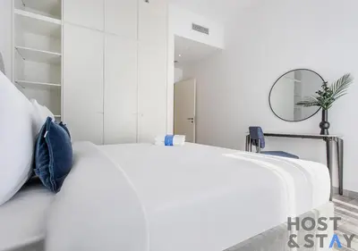 a white bedroom with a bed and a mirror at Unique 1BR in Belgravia Square, JVC - Host & Stay in Dubai