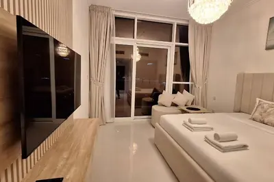 a white living room with a couch and a tv at Damac Hills Carson C studio with full kitchenet - Ideal for monthly stay in Dubai