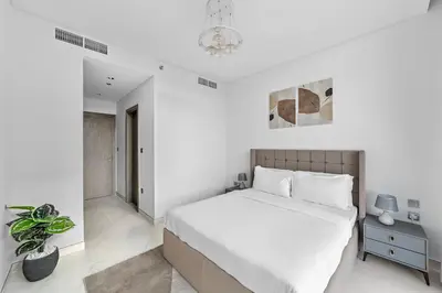 a white bedroom with a large bed and a plant at ALiving Classy 2BR I Lagoons View I District One Residence 7 in Dubai