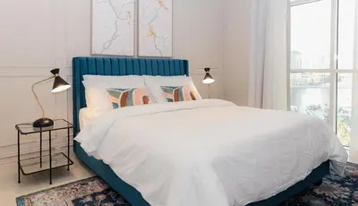 a white bed with a blue headboard in a bedroom at Prime Spacious 2 BR Apt, Burj Khalifa & Canal View - Scala Tower in Dubai
