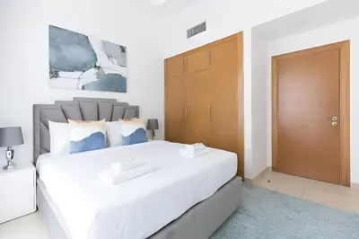 a bedroom with a large white bed with a wooden door at SkylineOasis1BR apt with BurjKhalifa & CanalView in Dubai