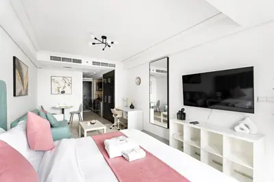 a white bedroom with a large bed and a living room at StoneTree - Cozy Studio - JLT in Dubai