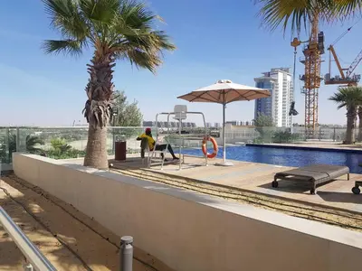 a man is sitting under an umbrella near a pool at Cosy 1 Bedroom in Damac Hills | OFEX in Dubai