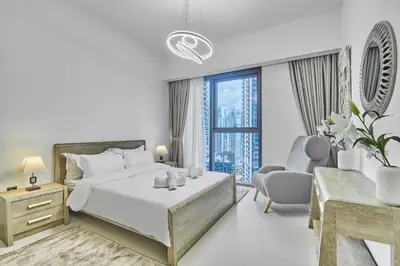 a white bedroom with a bed and a chair at MAJESTIC Act Two 2BR- 27th Floor Burj Khalifa- Downtown Dubai in Dubai