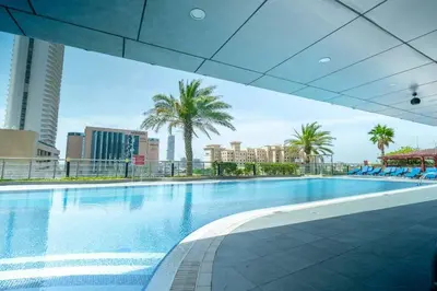 a large swimming pool with palm trees and buildings at Cozy Spacious Apartment 1BR in Dubai