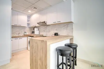 a kitchen with white cabinets and black stools at Special Offer Stylish 1BR with Scenic Views & Pool by Deluxe Holiday Homes in Dubai