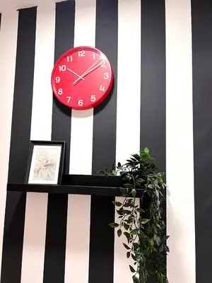 a red clock on a striped wall with a plant at Deluxe Couple Partition Room in Tecom Near Metro in Dubai