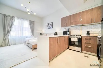 a kitchen with wooden cabinets and a bed in a room at Stylish Studio Apartment at Casa Grande, JVC by Deluxe Holiday Homes in Dubai