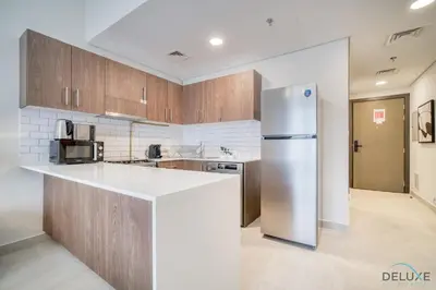 a kitchen with a refrigerator and wooden cabinets at Stylish Studio Apartment at Casa Grande, JVC by Deluxe Holiday Homes in Dubai
