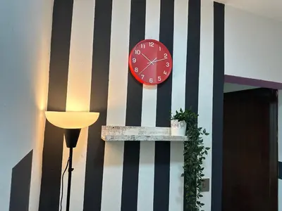 a red clock on a striped wall next to a lamp at Prime Partition Room in Al Barsha 1 Near Metro in Dubai