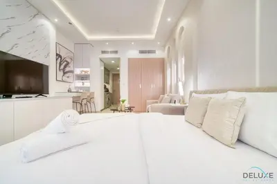 a white bedroom with a large bed and a kitchen at Pleasant Studio Apartment at Azizi Riviera 13, Al Merkadh by Deluxe Holiday Homes in Dubai