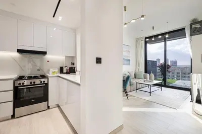 a kitchen with white cabinets and a view of a living room at Spacious Balcony, King Bed, Pool at JVC Dubai in Dubai