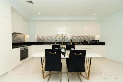 a white kitchen with a table and chairs at Oraya - Paramount Midtown Luxurious 2BR with Sea View in Dubai