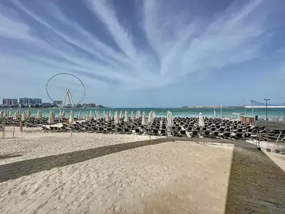 a beach with chairs and a ferris wheel in the background at La Vie, JBR - Cosy Two Bedroom in Dubai