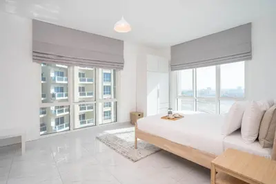 a white bedroom with a bed and large windows at Budget Friendly Production City in Dubai