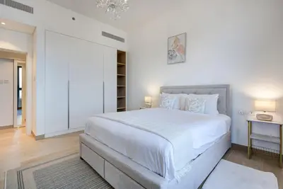 a white bedroom with a large bed and a chandelier at Trophy - Serene Abode near the Coast in Dubai