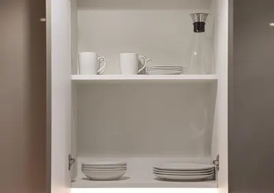 a white pantry with plates and cups and dishes at 1BR Gem with Pool 15 Mins to Downtown Dubai in Dubai