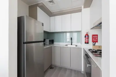 a kitchen with white cabinets and a stainless steel refrigerator at Fresh & Quiet 1BR at Midtown Noor 4 Tower in Dubai