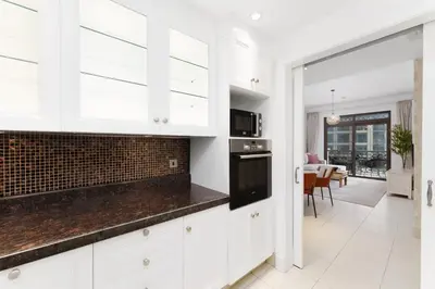a kitchen with white cabinets and a living room at Green living chic 1 bedroom apartment in Dubai