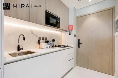 a white kitchen with a sink and a door at Mira Holiday Homes-Cozy studio close to metro in Dubai
