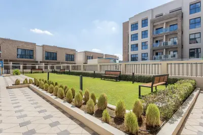 a park with benches and bushes in front of buildings at Holiday Studio In JVC 0107, Dubai in Dubai